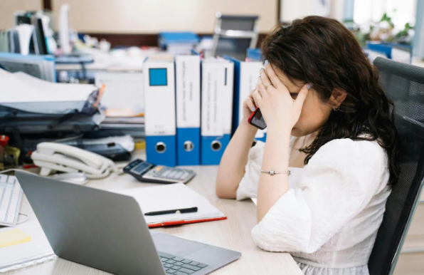 Woman at desk with head in hands — emotional suppression at work